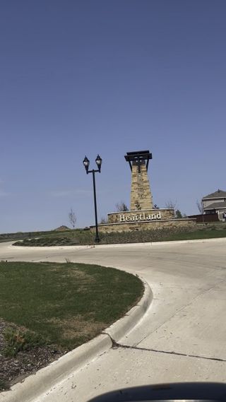Street view A welcoming entry feature with a stone pillar and lantern lights in Heartland Signature by KB Home (Heartland, TX).