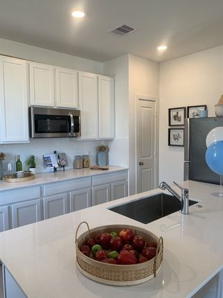 Model Home A modern kitchen with sleek white cabinetry, stainless steel appliances, and a spacious island featuring a basket of apples.