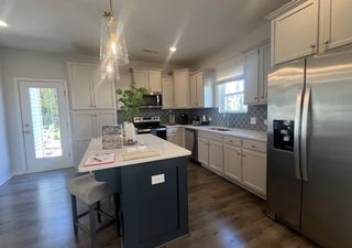 A modern kitchen with white cabinetry, stainless steel appliances, a central island, and elegant pendant lighting.