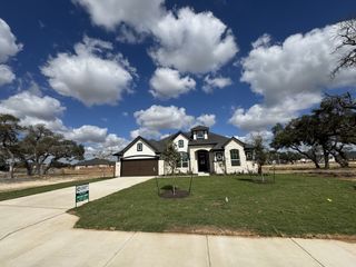 A stunning stone home with a spacious driveway and lush lawn in Broken Oak by Chesmar Homes (Georgetown, TX).