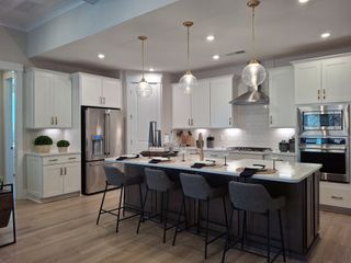 Model Home A modern kitchen with sleek white cabinets, a large island, pendant lighting, and stainless steel appliances.