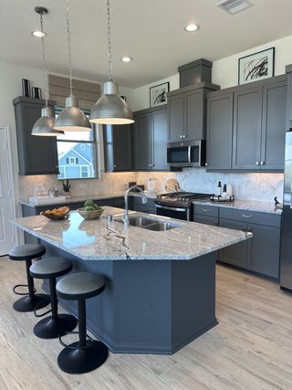 A modern kitchen with sleek gray cabinets, a granite island, and stylish pendant lighting.