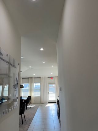 Model Home A bright hallway with tiled flooring, leading to a sunlit room with large windows and white curtains, offering a cozy ambiance.