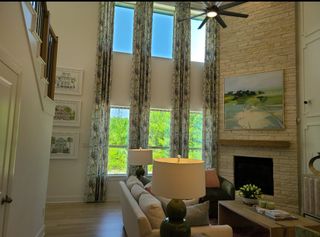 A spacious living room with high ceilings, tall windows, a brick fireplace, and elegant decor.