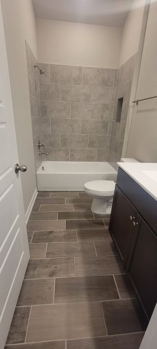A sleek bathroom featuring a tiled bathtub, modern vanity, and wood-style flooring.