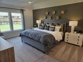 A cozy bedroom with a plush grey bed, accent wall, dual nightstands, and large windows overlooking a backyard.