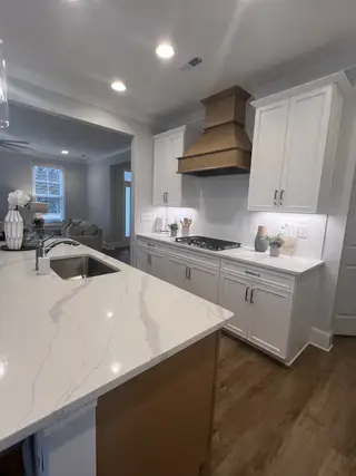 Model Home A contemporary kitchen featuring sleek quartz countertops, a bronze range hood, and elegant white cabinetry.