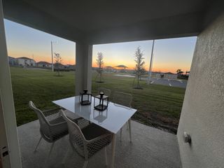 A cozy patio with a modern table and chairs, offering a serene view of a sunset over lush green lawns.
