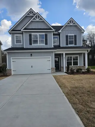 A charming two-story home with light gray siding, black shutters, and a spacious driveway stands proudly in The Hills at Cedar Creek by Direct Residential Communities (Winder, GA).