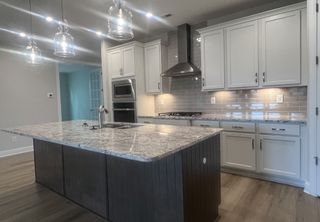 Model Home A modern kitchen with a granite island, stainless appliances, and pendant lighting creating a sleek and inviting space.