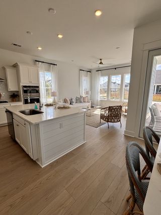 A bright and airy kitchen-living space with wood floors, large windows, and modern white cabinetry.