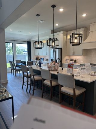 Model Home A modern kitchen with pendant lighting, white cabinetry, and a spacious island with seating, opening to a dining area.