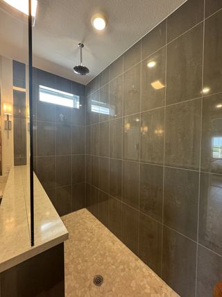 A modern walk-in shower with sleek gray tiles and pebble flooring, accented by elegant lighting and a rainfall showerhead.