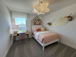 Model Home A cozy bedroom with a playful "hello" decor, pink bedding, desk, and modern lighting.