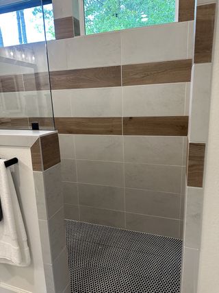 A modern shower with wood-accented tiles and a pebble mosaic floor, offering a serene and stylish bathing experience.