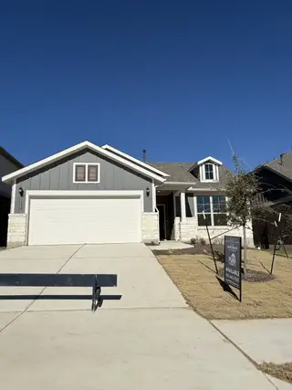 Street view A charming grey home with a white garage and manicured lawn in Saddleback at Santa Rita Ranch by Pulte Homes (Liberty Hill, TX).
