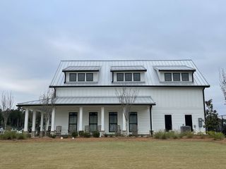 A modern white farmhouse with a metal roof, porch, and landscaping in Homecoming by True Homes (Ravenel, SC).