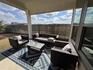 A covered outdoor living space with modern wicker seating, stylish décor, and a view of the private fenced backyard.