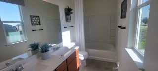A bright bathroom in a Marbella home, featuring dual sinks, a combination tub and shower, and natural light from two windows (San Antonio, TX).