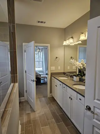 A sophisticated bathroom featuring dual sinks, modern lighting, and wood-style tiled flooring.