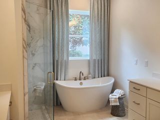 A luxurious bathroom with a marble-accented glass shower, freestanding tub, and soft drapery for a spa-like retreat.