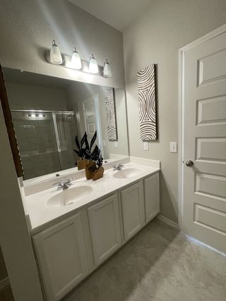 Model Home A modern bathroom with dual sinks, a large mirror, sleek cabinetry, and decorative wall art.