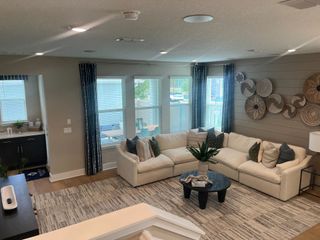 A cozy living room features a large beige sectional, modern decor, and ample natural light through wide windows.