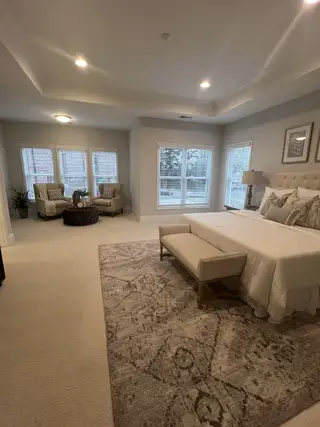 Model Home A spacious bedroom with plush seating, elegant decor, and natural light from large windows.