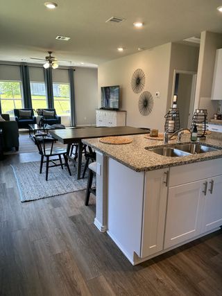 Model Home An open-concept living area featuring wood floors, a granite kitchen island, and a cozy seating area with large windows.