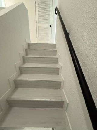A modern staircase with sleek white steps and a black handrail leading to a louvered door.