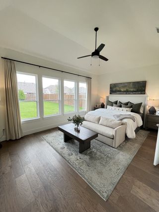 A serene bedroom with a comfy bed, soft rug, large windows, and sleek ceiling fan.