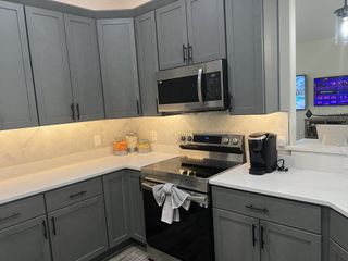A modern kitchen with sleek gray cabinets, herringbone backsplash, and stainless steel appliances.