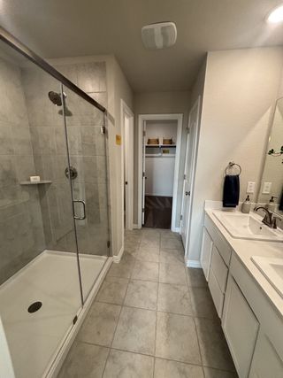 A bright bathroom with a large walk-in shower, dual sinks, and tiled flooring in Red Hawk Landing by HistoryMaker Homes (San Antonio, TX).