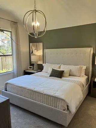A cozy bedroom with a tufted bed, warm lighting, and an elegant chandelier, complemented by a sage green accent wall.