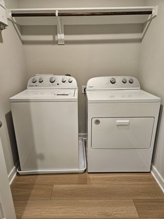 Model Home A functional laundry room with white washer, dryer, and a wooden shelf, featuring sleek wood-look flooring.