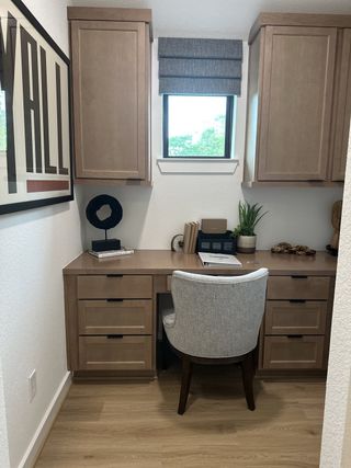 A cozy home office nook with wooden cabinetry, a plush chair, and natural light filtering in through a small window.