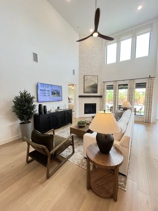 A modern living area with a high ceiling, elegant fan, cozy fireplace, and sleek furnishings.