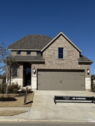 Street view A charming brick home with a peaked roof and inviting driveway in Santa Rita Ranch by Perry Homes (Liberty Hill, TX).