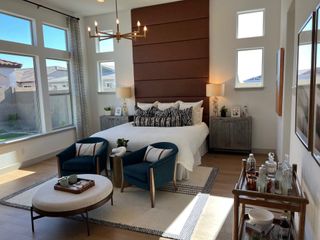 Model Home A cozy bedroom with large windows, a modern chandelier, plush seating, and stylish decor, creating a warm and inviting space.