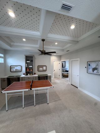 A spacious game room with a ping pong table, coffered ceiling, and built-in desks for entertainment and productivity.