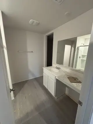 A bright bathroom with sleek flooring, white cabinetry, and an expansive mirror for a modern touch.