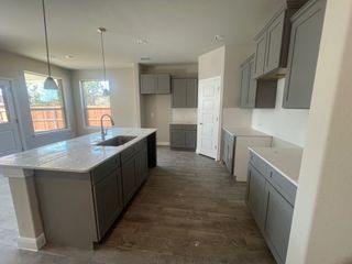 Model Home A modern kitchen featuring gray cabinetry, a large island with sink, and ample natural light through wide windows.