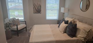 A cozy bedroom with a neutral palette, plush bedding, a sleek armchair, and soft natural light streaming through blinds.