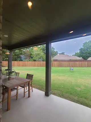 Model Home A cozy patio with wooden dining set, overlooking a spacious fenced backyard and lush greenery.