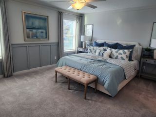 Model Home A serene bedroom with cozy blue bedding, elegant wainscoting, a tufted bench, and stylish artwork.