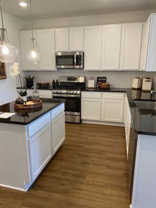 A modern kitchen with white cabinets, stainless steel appliances, dark granite countertops, and pendant lighting over an island.