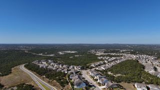 Aerial view of scenic homes amidst lush greenery in Headwaters 50' - Executive Series by David Weekley Homes (Dripping Springs, TX).
