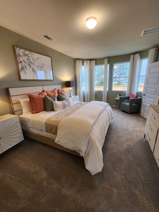 A cozy bedroom with a plush carpet, elegant bed, warm lighting, and large windows offering a serene view.