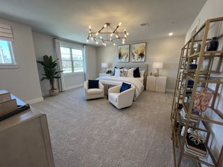 A spacious bedroom featuring plush carpet, modern chandelier, cozy seating, and elegant decor in soft tones.