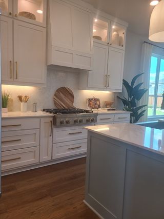 A modern kitchen featuring white cabinets, gold hardware, and wooden floors, illuminated with natural and under-cabinet lighting.